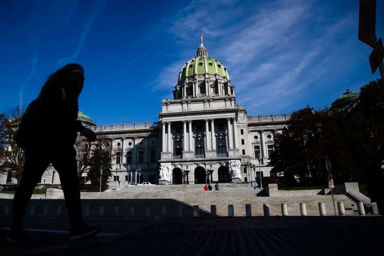 A man is silhouetted in the shade as he walks by the Pennsylvania Capitol in Harrisburg, Pa.