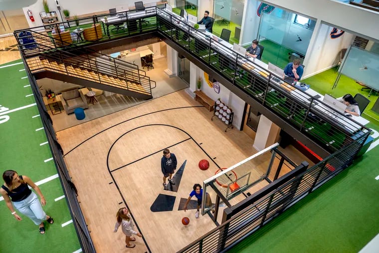 The two-story atrium with basketball court on the ground floor and workstations around the upper floor at the headquarters of Playfly Sports in a renovated former roller rink and theater in downtown Berwyn.