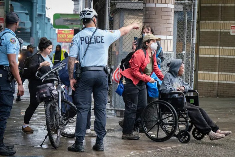 A person in a wheelchair who was escorted from the encampment on Kensington Avenue is directed away from the encampment by Philadelphia police on Wednesday.