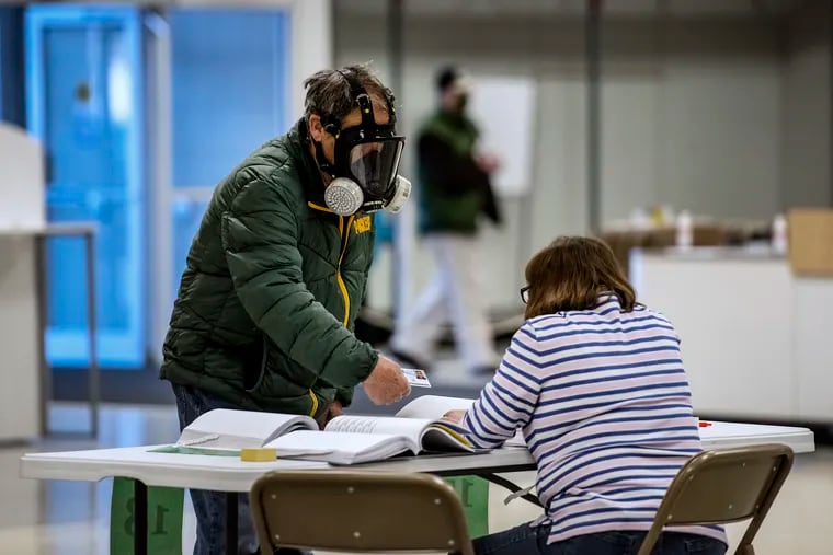 Robert Forrestal, left, wears a full face chemical shield to protect against the spread of coronavirus, as he votes Tuesday, April 7, 2020, at the Janesville Mall in Janesville, Wis. Hundreds of voters in Wisconsin are waiting in line to cast ballots at polling places for the state's presidential primary election, ignoring a stay-at-home order over the coronavirus threat.