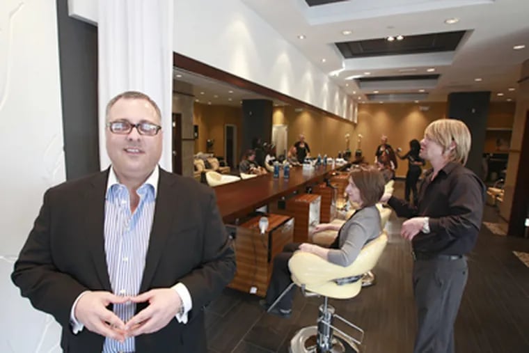 Owner Anthony Rossano in his new b2 salon in Phila., where stylist Jason Althouse works with Terri McDevitt's hair. (David Swanson / Staff Photographer)