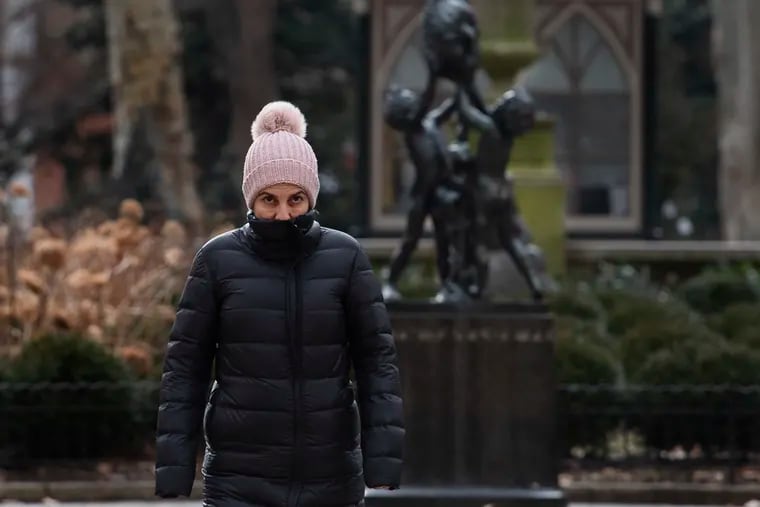 A pedestrian shields from the cold air as temperatures began to drop in Rittenhouse Square on Sunday.
