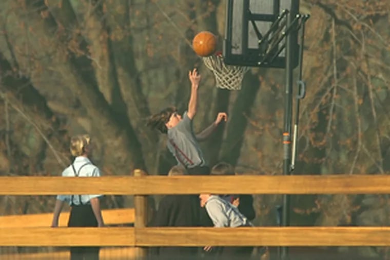 Amish children play basketball on the playground of their new schoolhouse. The community had considered installing electrical security devices in the new building but opted to stick with tradition.
