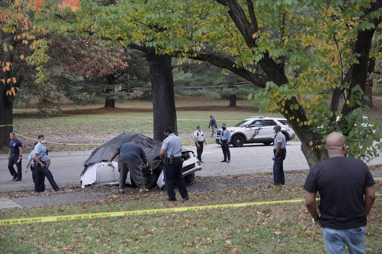A tarp covers a car that crashed, reportedly killing two people, along Belmont Avenue in Philadelphia's West Fairmount Park on Saturday, Oct. 24, 2020.