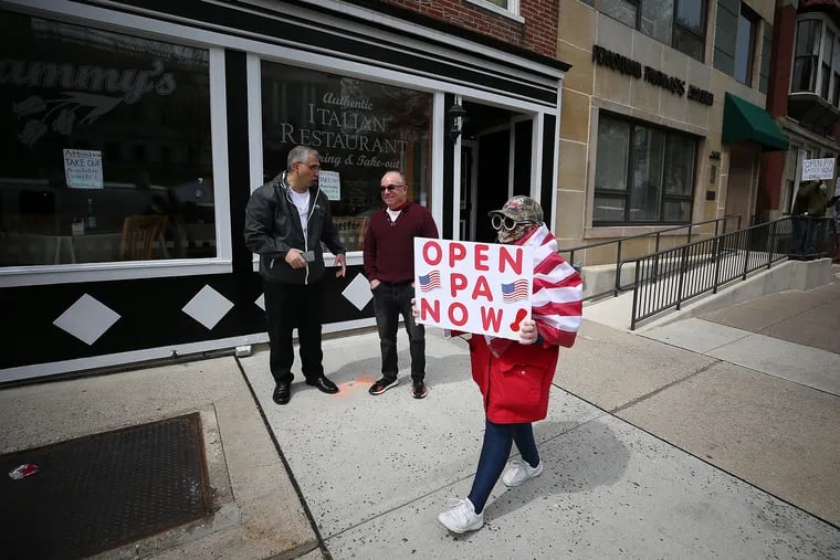 File photo shows a protester walking by a restaurant as fellow protesters gather outside the Capital Complex in Harrisburg, calling on Gov. Wolf to reopen up the state's economy during the coronavirus outbreak.