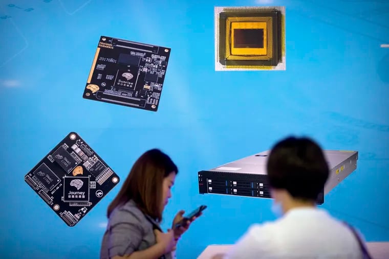 Visitors walk past a display showing microchips and circuit boards at a 2018 technology exhibition in Beijing. China is investing billions to surpass the U.S. in both civilian and military uses of chips. Trudy Rubin writes that China would also like to control the world's largest chip producer, Taiwan.