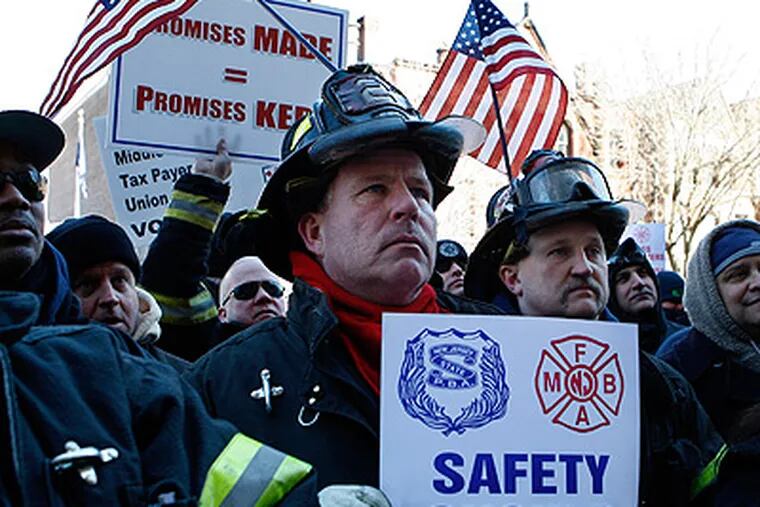 Elizabeth Fire Department firefighters Rick Maliniak, center left, and Andy Socha have American flags stuck in their helmets as they stand with other firefighters and police officers and their supporters in a large gathering outside the Trenton Statehouse on Thursday during a rally to protest staff cuts and promote public safety. (Mel Evans / Associated Press)