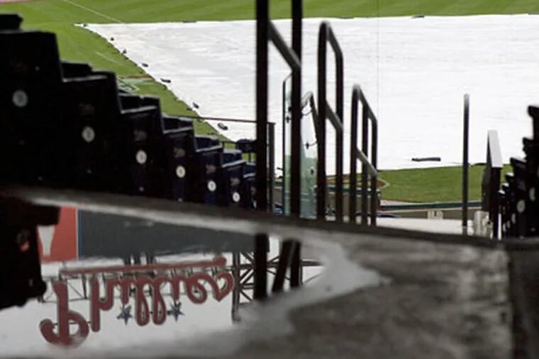 The Phillies sign on the scoreboard is shown reflected in a puddle next to some seats, and the baseball field had a tarp over it at Citizens Bank Park on Tuesday. Game 5 of the World Series may resume tonight, weather permitting. (Jessica Griffin / Staff Photographer)