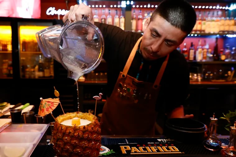 Bartender Alejandro Vaca pours a Piña Colada into a pineapple served at Tamalex Bar & Grill in the Society Hill neighborhood of Philadelphia on Friday, February 8, 2024.  The piña colada is made with Plantation Run, pineapple, lime and coconut cream.