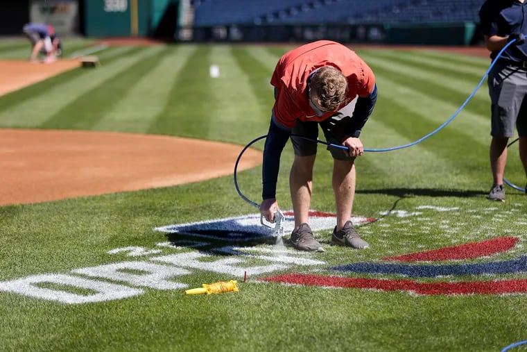 Jeremy Wilt, manager of field operations, paints the “Opening Day” logo on the field at Citizens Bank Park. Phillies manager Joe Girardi is thrilled that fans will be back in the ballpark for the 2021 opener and season.