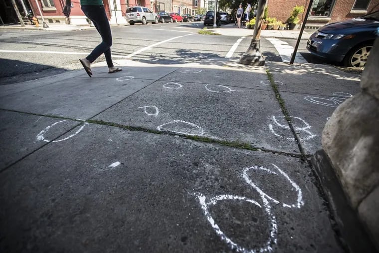 On Sunday morning, July 16, 2017, a pedestrian walks by the sidewalk at 22nd and Fitzwater that is marked up with chalk circles indicating where police found shell casings, 34 in all, from a gun fight that happened around midnight Saturday night.