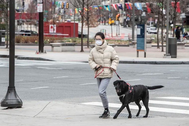 A woman walks her dog across JFK Blvd in a nearly deserted Love Park and Dilworth Plaza on Sunday March 22, 2020, hours before a citywide "stay at home" order was to take effect in Philadelphia amid the coronavirus outbreak.