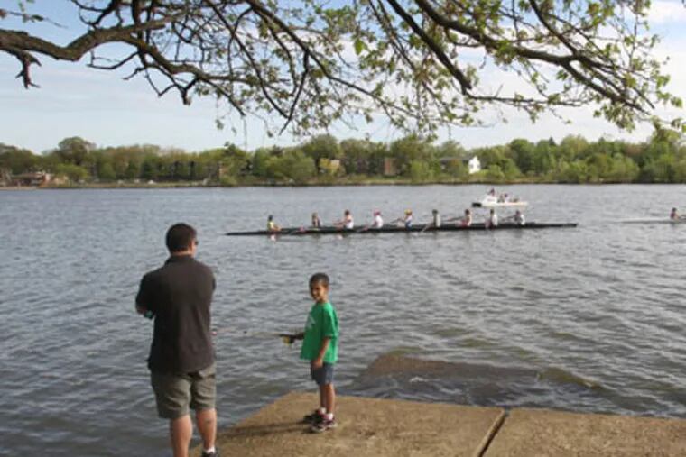 A young boy fishes while crew teams practice on the Cooper River at Cooper River Park in 2012. ( Charles Fox / Staff Photographer )