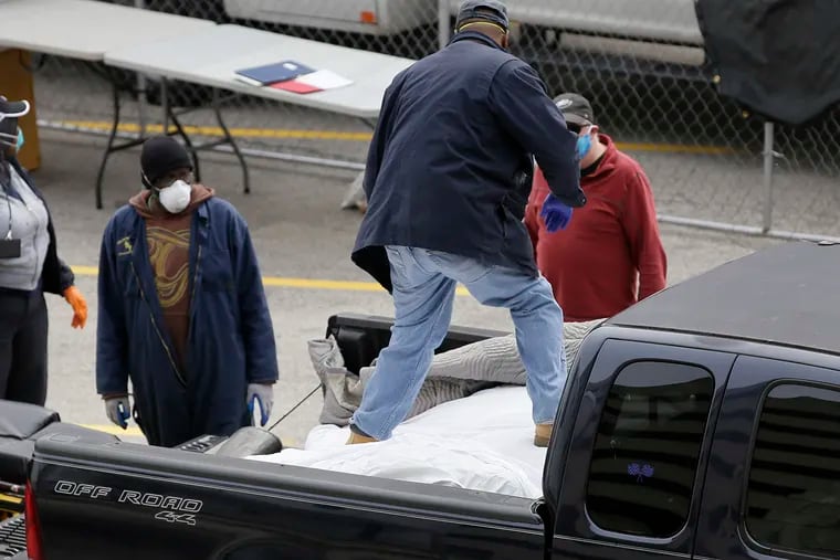 As workers look on, the driver of a pick-up truck stands on the bodies in the cargo bed as he uncovers them from beneath a mat.