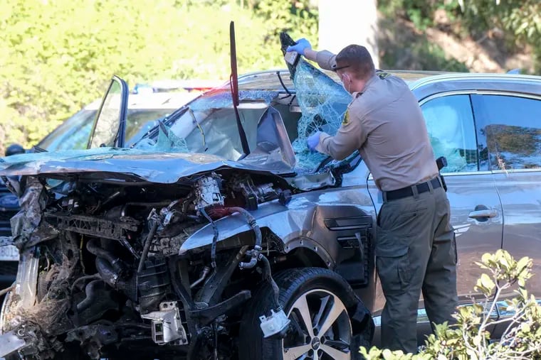 A police officer investigates a damaged car being driven by Tiger Woods after an accident in Los Angeles on Tuesday.