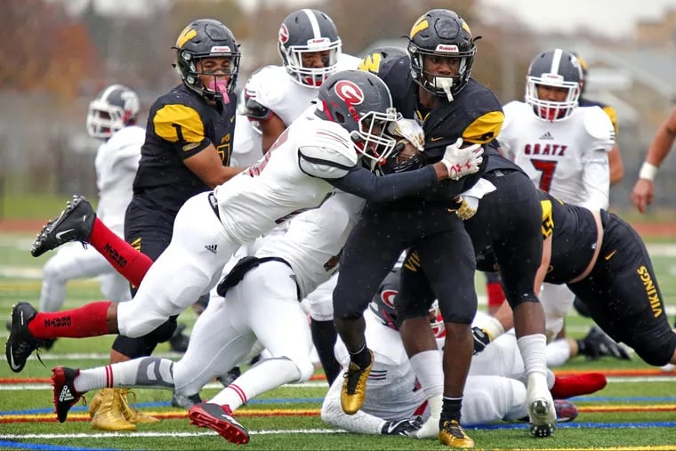 Archbishop Wood’s Nasir Peoples carries Simon Gratz defenders Jawon Harrison (middle, airborne) and Terrell Stewart (hidden) for yardage in Saturday afternoon’s PIAA District 12 Class 5A football final.