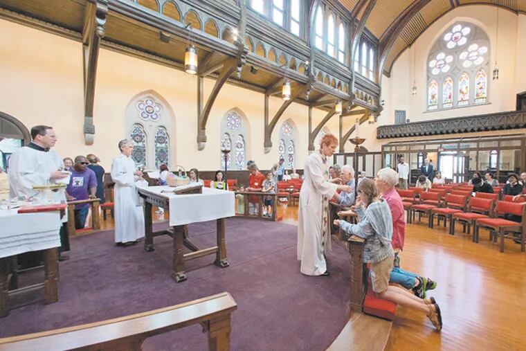 The Rev. Donna L. Maree offers communion during a mass to recognize the 20th anniversary of lighting strike, fire and rebuilding of Trinity Memorial Church, Spruce St., Philadelphia, July 27, 2014. (DAVID M WARREN/Staff Photographer)