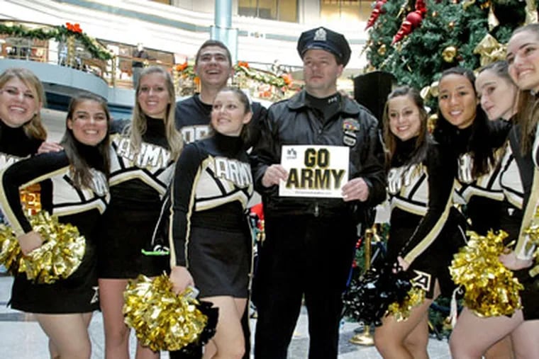 Philadelphia Police Officer Mark Strange poses with the Army Cheerleaders after a pep rally and "Hole-in-One Challenge" at The Shops at Liberty Place Friday leading up to Saturday's Army-Navy football game. (Tom Gralish / Staff Photographer)