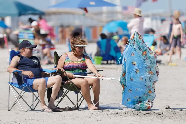 A couple of Wildwood beach visitors fight the wind for control of their umbrella a few weeks back. Winds were gusting past 20 mph on Saturday.