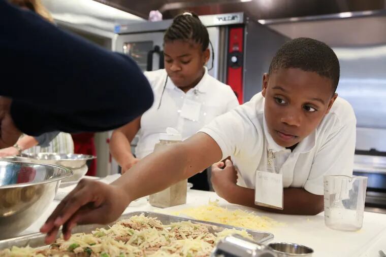 Samiek Miller, 11, sprinkles cheese on top of the tuna melts, one of the final steps before they're placed in the oven to bake. Behind him, Dayanna Shomo, 11, works on the zucchini fries.