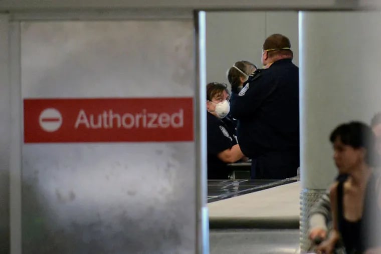 Masked customs officers look on during a screening area for international passengers from United flight 998 from Brussels at Newark airport in Newark, N.J., Saturday, Oct. 4, 2014. New Jersey health officials say Ebola has been ruled out as the cause of illness for a man who became sick on a flight from Brussels to the United States (AP Photo/Northjersey.com, Viorel Florescu)