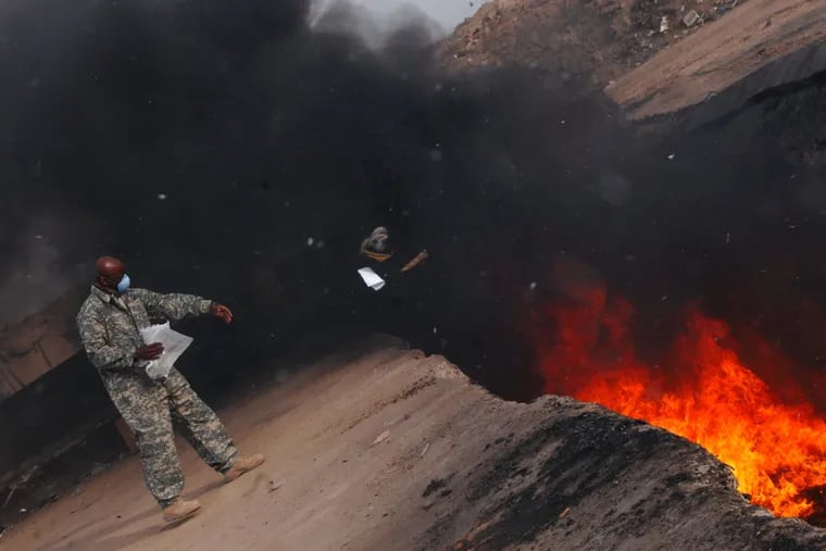 An Air Force service member tosses items into a burn pit at Balad Air Base, Iraq, in March 2008.