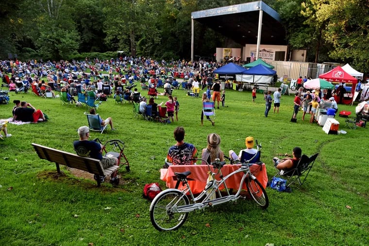 Northeast Philadelphia music lovers Ed Rehl (left), 60; and Janet Heiser (left), 56;  sit in front of the vintage Schwinn tandem bicycle they rode to the summer Wednesday night Pennypack Park Music Festival free concert July 24, 2019, where Starman, a tribute band playing the music of David Bowie performs on the Ed Kelly Amphitheater stage. Heiser came to concerts there in the 1980s with her mother when her children were toddlers. "It was big bands in those days, and we even had Al Alberts play here." (Alberts was a Philadelphia music star. He formed the Four Aces in the 1950s, and later recorded "On the Way to Cape May," still a Jersey Shore classic. Even later he hosted a Saturday afternoon talent TV show for youngsters called Al Alberts Showcase.