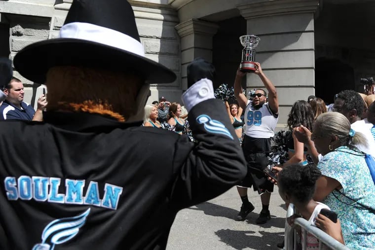 The Philadelphia Soul mascot, Soulman, cheers as defensive lineman Justin Lawrence carries the 2017 AFL championship trophy.