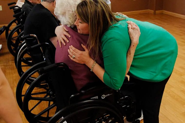 Staff member Stacy Omar hugs a resident during a memorial service at the center. An administrator said residents were asking for more opportunities to express their wishes, now that they know staff is listening. ( Bradley C Bower / For the Inquirer )