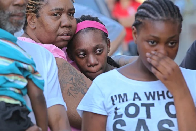 Phyllis Myers, left, the grandmother of the 4-year-old girl that was allegedly shot by her father in Kensington, holds on tight to another granddaughter as she and other family members participate in a prayer vigil in front of the family's home on Monday afternoon.