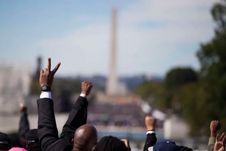 People raise their arms as they mark the 20th anniversary of the Million Man March in Washington. Saturday's event reflected the growing anger and tension over recent killings by police.