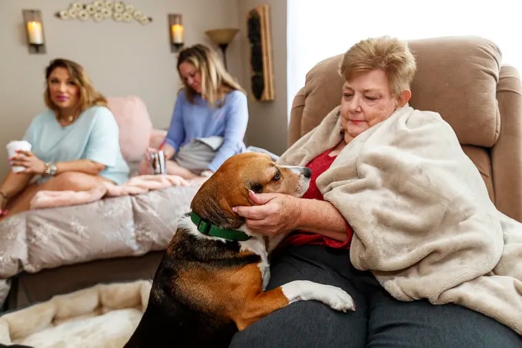 Lynn Schutzman, right, a former pharmacist who was living homeless in King of Prussia, comforts her pet beagle, Chaucer, while Melissa Akacha (left) and Jennifer Elsie keep her company in her new apartment. Akacha and Elsier coaxed Schutzman to accept help.