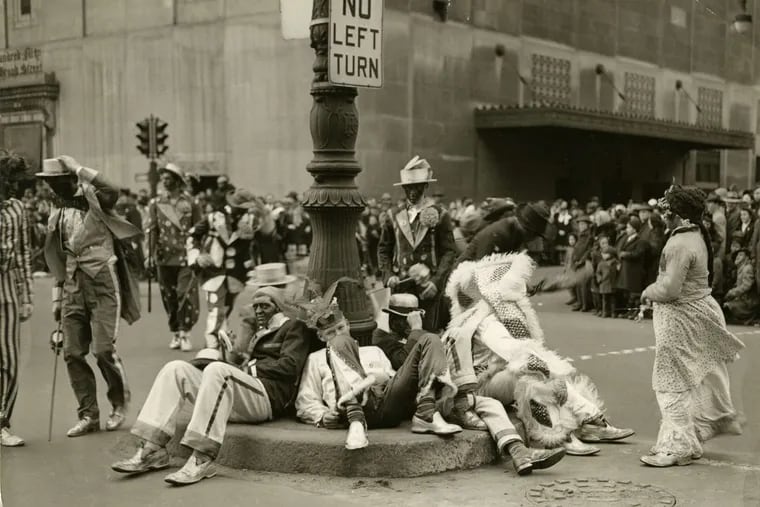 Mummers, including dudes in blackface, sit around the pole of a street sign during the parade in 1946.