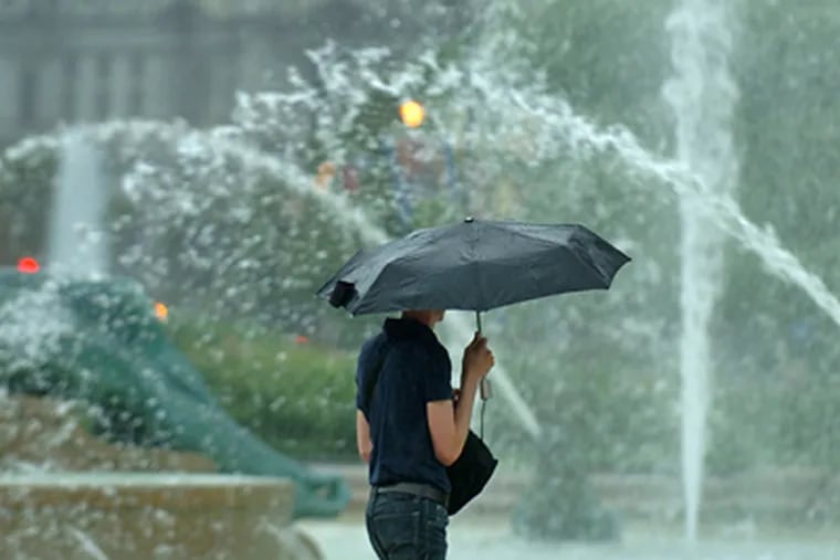 In an appearance that’s only slightly deceiving, a woman seems to walk through the Swann Fountain on Logan Circle during one of yesterday’s showers. (Clem Murray / Staff Photographer)