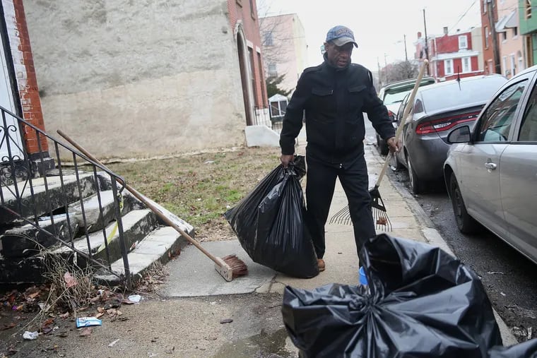 Ernest Gardner carries a bag of trash after raking it off of his block on North 19th Street in North Central Philadelphia in February.