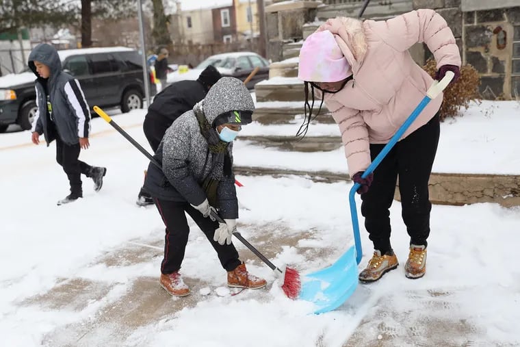 Breden Holmes (left), 5, sweeps snow into the shovel of Shayla Smith, 12, as they help clear the sidewalk outside their grandmother's home on 46th Street in West Philadelphia during a winter storm that brought snow and sleet to the Philadelphia region on Feb. 18, 2021.