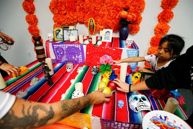 Thalia Vasquez (right) helps place objects on the Day of the Dead altar assembled at Juntos in South Philadelphia, which honors children who died while trying to cross the southwest border. At rear are photos of some of the children who have died.