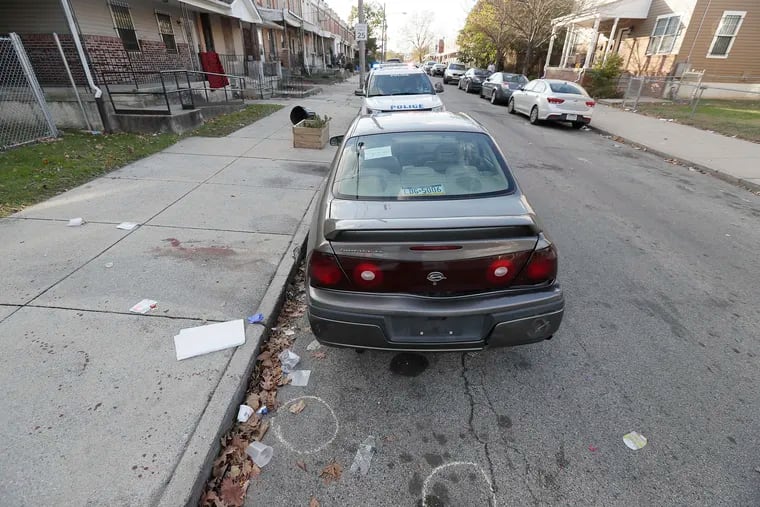 Circles on the 5500 block of Pearl Street in West Philadelphia indicate where shell casings were found after a shooting Sunday that wounded a 14-year-old and left a 23-year-old man dead. Police later towed the Chevrolet Impala pictured here as evidence.