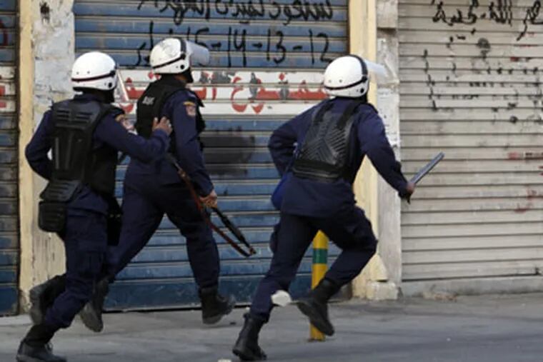 Riot police chase anti-government protesters, unseen, in Sanabis, Bahrain, on the edge of the capital of Manama on Sunday, Feb. 12, 2012, as protesters' attempts were thwarted to head toward an area nearby they call "Martyrs Square" that had served as the main hub for last spring's pro-democracy uprising. Writing on the garage door reads: "We will return to Martyrs Square 12-13-14-15 February." Bahrain on Sunday deployed thousands of security forces to confront anti-government protesters ahead of the one-year anniversary of the start of the Shiite-led uprising that seeks to loosen the ruling Sunni dynasty's monopoly on power. (AP Photo/Hasan Jamali)