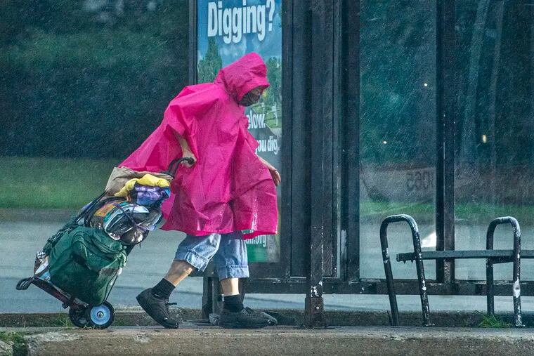 A pedestrian seeks shelter from heavy rain at a bus stop in Springfield, Pa., on Thursday.