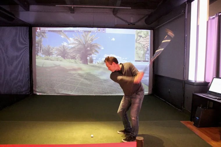 Owner Rick Troost takes a swing at a golf ball in one of his 18-foot-wide simulators at Golf &amp; Social, 1080 N. Delaware Ave.