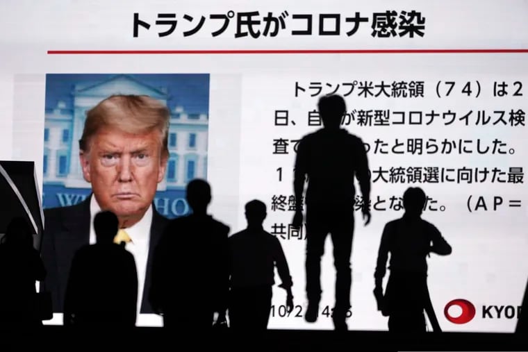 People in Tokyo walk past a screen showing the news report that President Trump has tested positive for the coronavirus.