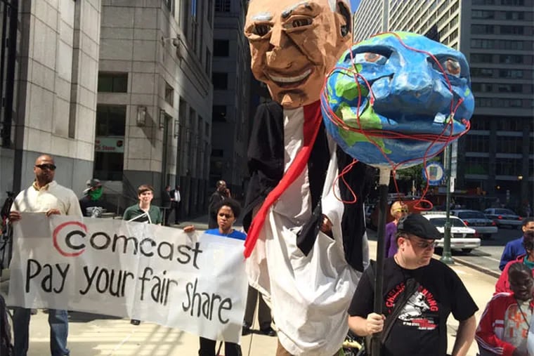 Demonstrators opposed to the merger of Comcast Corp. and Time Warner Cable Inc. and in favor of tighter FCC regulation of the Internet display puppets representing Comcast CEO Brian Roberts and a globe encircled by cable wires. Outside Comcast headquarters in Philadelphia, Sept. 15, 2014. (Bob Fernandez / Staff)