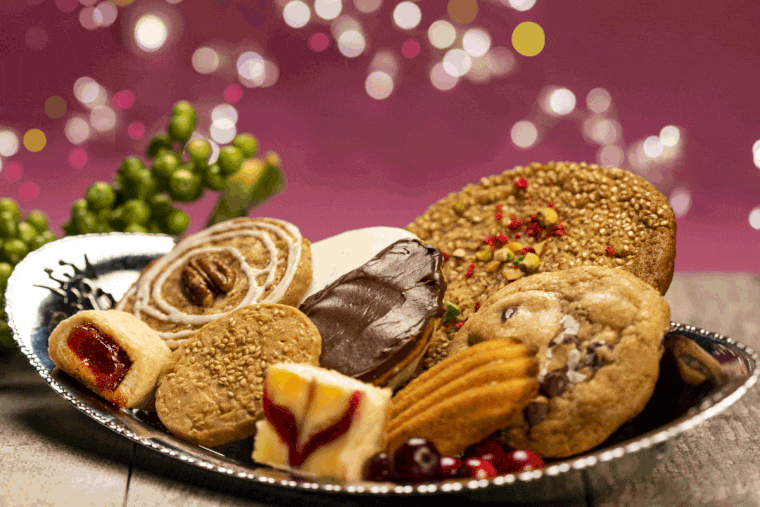 The 2023 holiday cookie assortment. Pictured are an assortment of eight cookies baked by Inquirer reporter Jenn Ladd. From right to left: sourdough chocolate chip cookie from Her Place Supper Club, madeleine from Mamie Colette bakery, caramelized butter and honey sesame cookie from Manna Bakery, black and white cookie from Essen Bakery, bourbon-pecan cookie from Small Oven Pastry Shop, cranberry swirl cheesecake bar from Flakely, cheddar-sesame crisp from Third Wheel Cheese Co,. and goiabinha (guava cookie square) from Merenda Box.