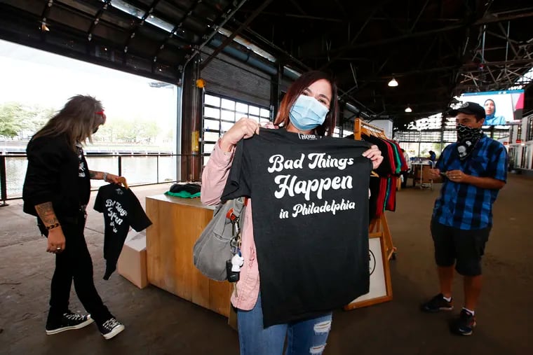 Customer Nadine Michael holds-up her Bad Things Happen in Philadelphia t-shirt as Do It Now T-Shirts owners Johnny Douglas (left) and Matt Charles prepare to sale their designed t-shirts at the Cherry St. Pier Fall Artist and Artisans Market on Friday, Oct 2, 2020.