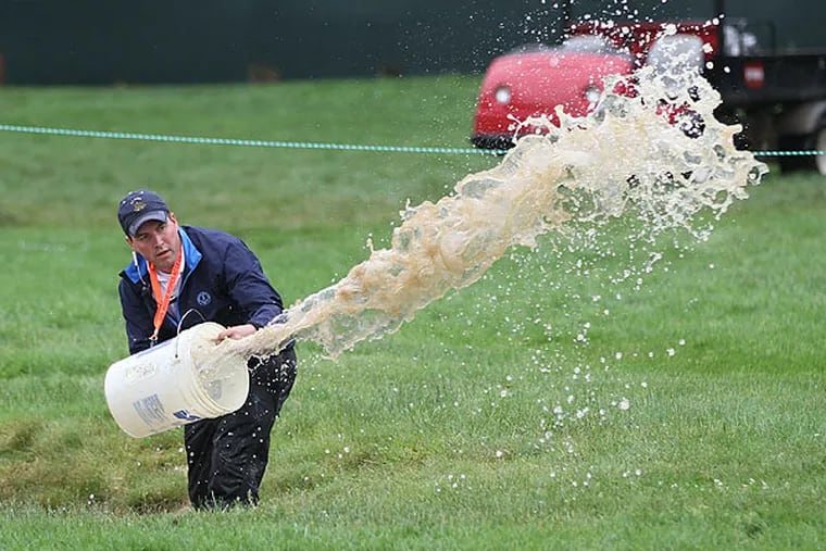 A Merion volunteer uses a five-gallon bucket to bail water out of a fairway bunker on the first hole after heavy rain on Monday morning. (Michael Bryant/Staff Photographer)