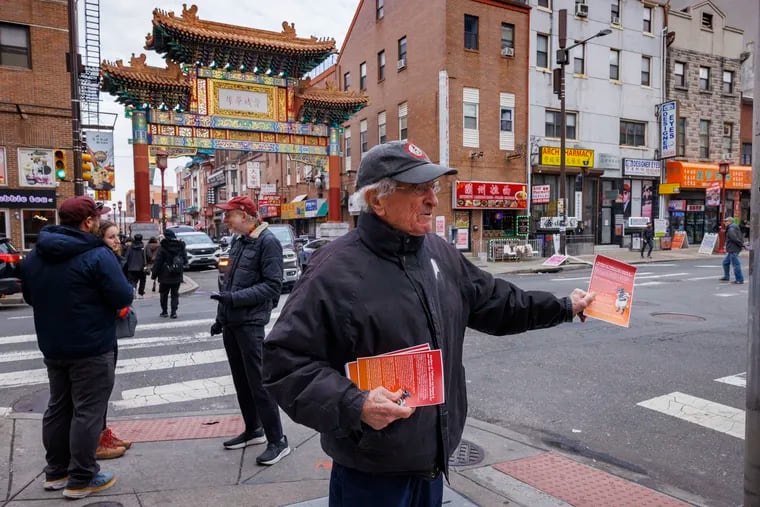 Harvey Finkle, documentary photographer hands out flyers along N. 10th Street to pedestrians during a Christmas day protest against Sixers building a new arena near Chinatown.  "No Arena in Chinatown" protesters hosted a "Christmas Caroling" rally on Christmas day, singing rewritten carols from what they call their "Chinatown Is Not Just A Place to Eat on Christmas" playbook.” Protesters gathered along Arch Street at N. 10th Street, Chinatown, Philadelphia.