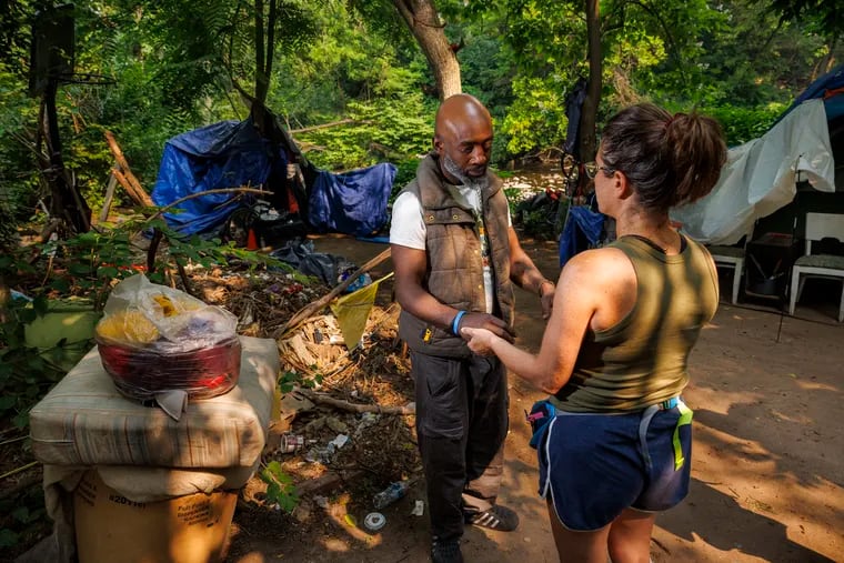 Ameen McCall, 42, holding hands with Stephanie Sena, Villanova professor and homeless advocate, at an encampment in Norristown in June. Sena and others plan to take complaints about how people who are living homeless in the borough have been treated to the United Nations.