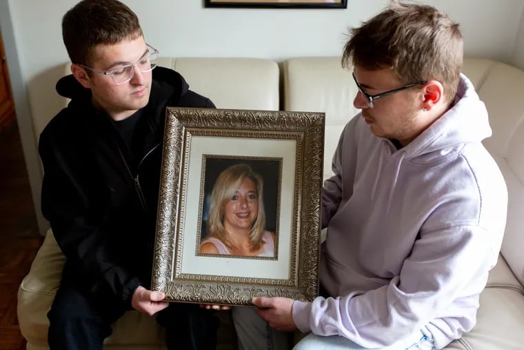 Anthony (left) and Angelo Delzingaro hold a portrait of their mother, Leslie Delzingaro, who was shot death in a Philadelphia tavern nine years ago. Both detectives tasked with solving the unsolved murder have been arrested on corruption charges.
