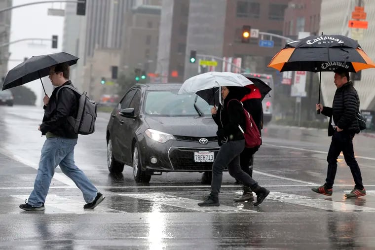 FILE - In this Monday, Feb. 6, 2017 file photo, pedestrians cross a rainy street in downtown Los Angeles. According to a study released in April 2019 in the Bulletin of the American Meteorological Society, even light rain significantly increases the risk of a fatal car crash. (AP Photo/Nick Ut)